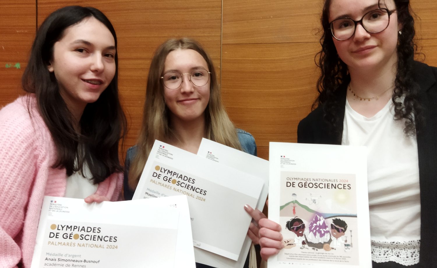Les élèves Maëline, Anaïs et Léna reçoivent la médaille d'argent lors des Olympiades nationales de géosciences à Paris, accompagnées de leur professeur, Mme Lucie Loyer, devant une exposition de minéraux à Sorbonne Université.